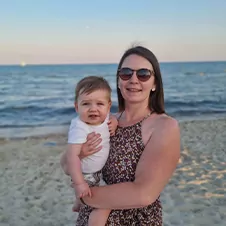 Een vrouw met een baby op een zandstrand, met de oceaan op de achtergrond.