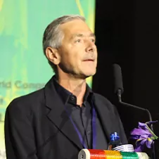 Een man in pak spreekt zelfverzekerd op een podium met een microfoon, omringd door een groene achtergrond die doet denken aan een frisse webdesigninspiratie.